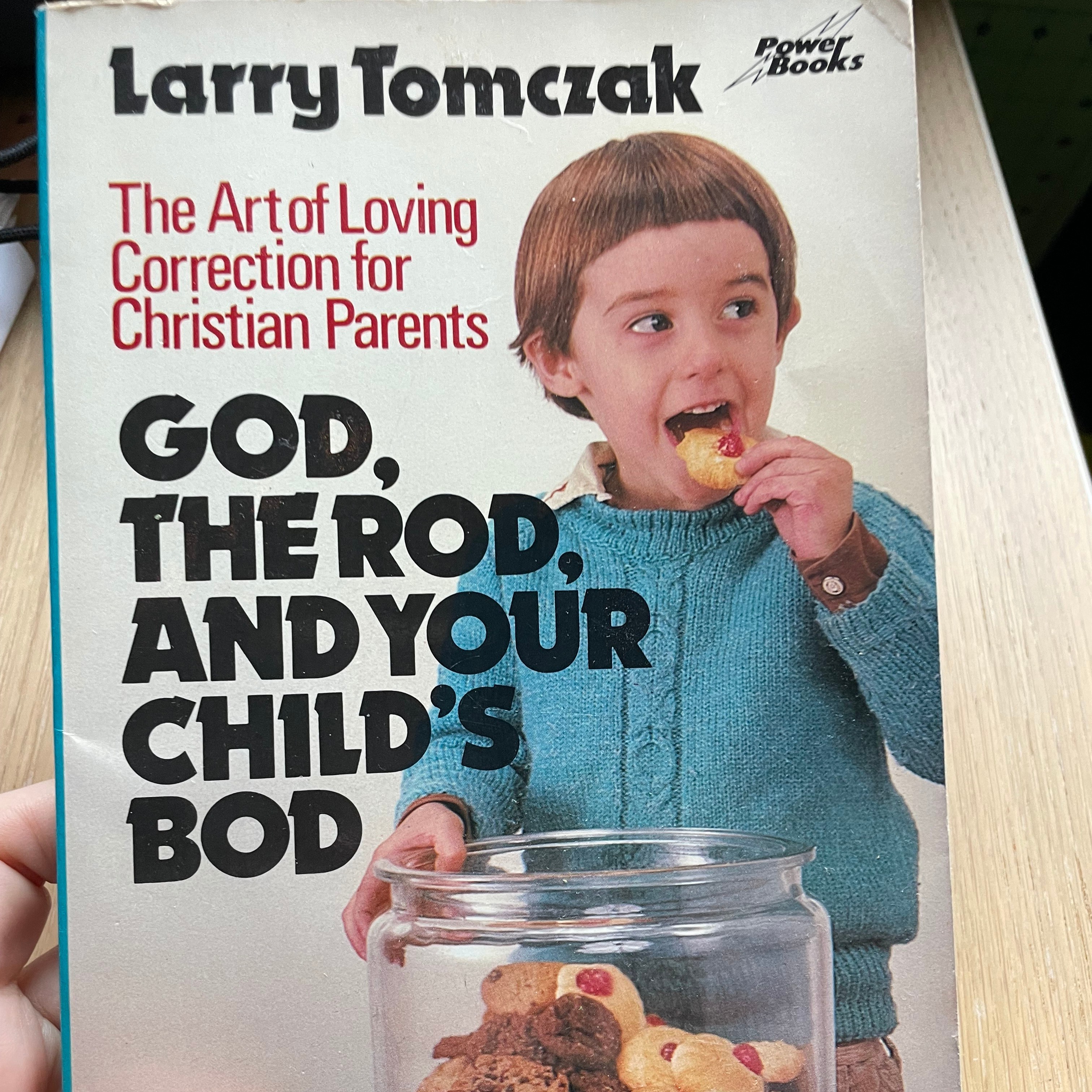an image of a book cover that says larry tomczakk the art of loving correction for Christian parents God, the rod and your parents bod with a boy with a bowl cut stealing a cookie from a cookie jar. He looks mischeivious but if you look closely you can see tears in his eyes